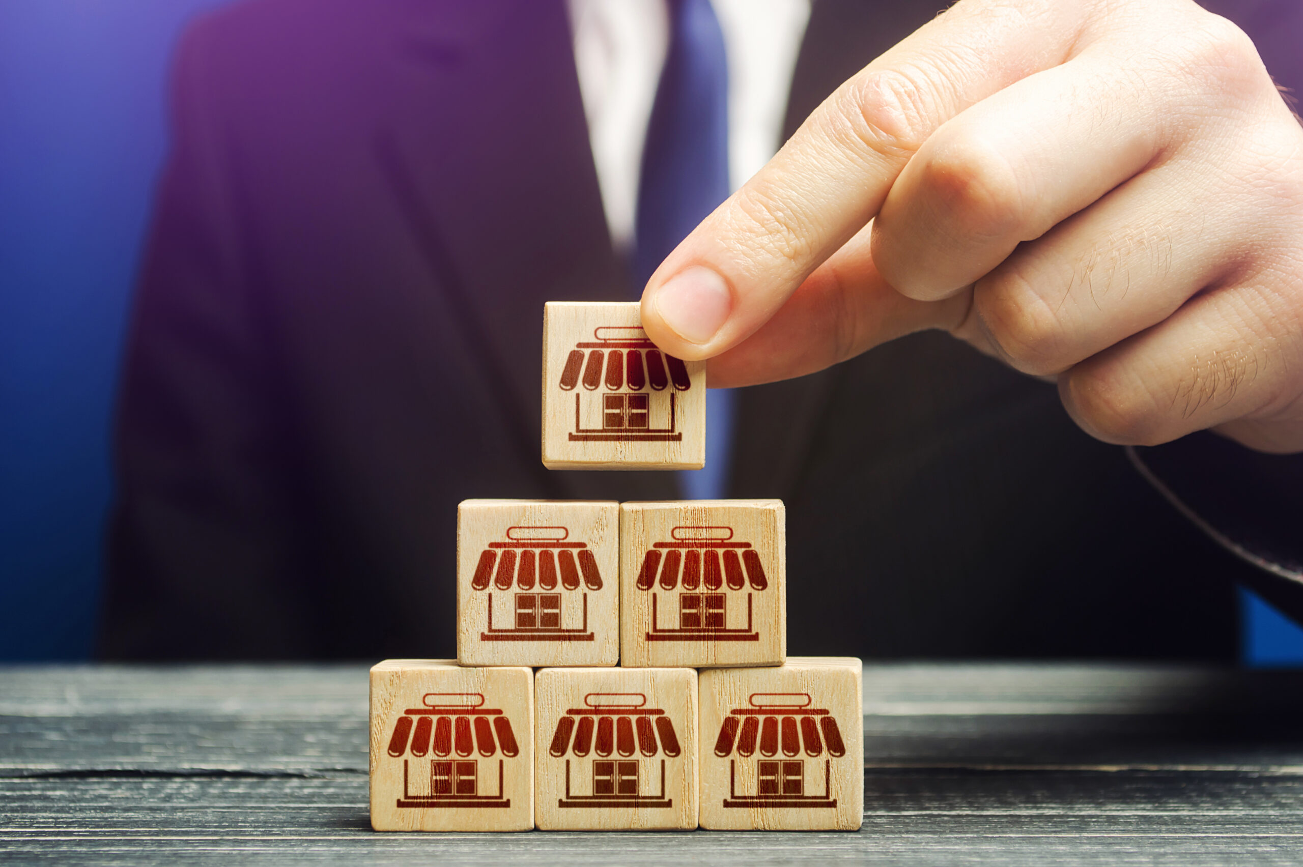 A man builds a pyramid from blocks of business shops. Building a successful business empire. Expansion and competitive growth. Franchise concession concept. Commercial network development.